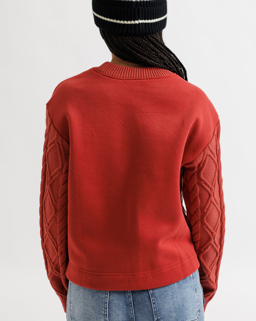 Person wearing a red sweater with cable knit sleeves on a plain background