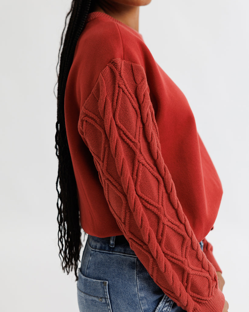 Person wearing a red cable knit sweater with a plain background