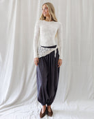 Model wearing an ivory semi-sheer lace-knit long-sleeve top featuring a subtle floral pattern and classic crew neckline, styled tucked into high-waisted plaid pants.