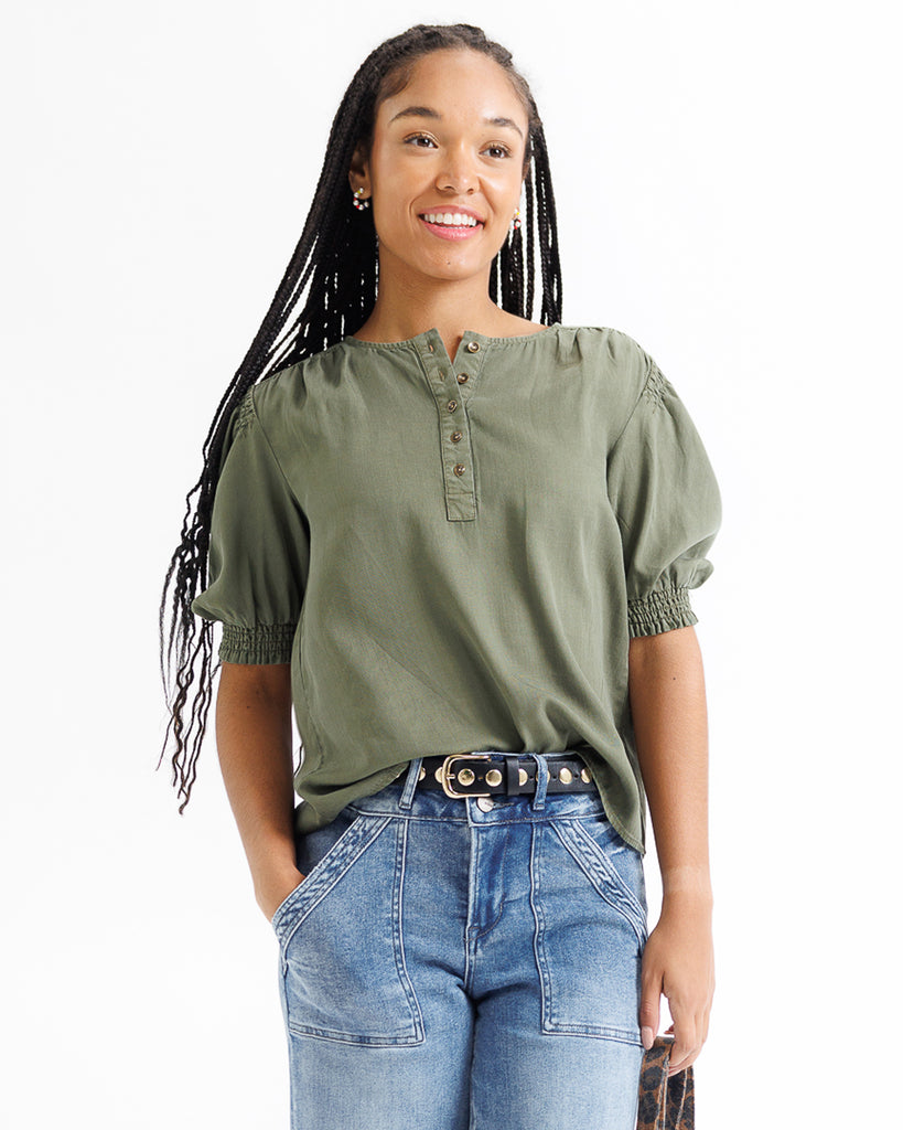 Woman wearing an olive green top and blue jeans on a white background