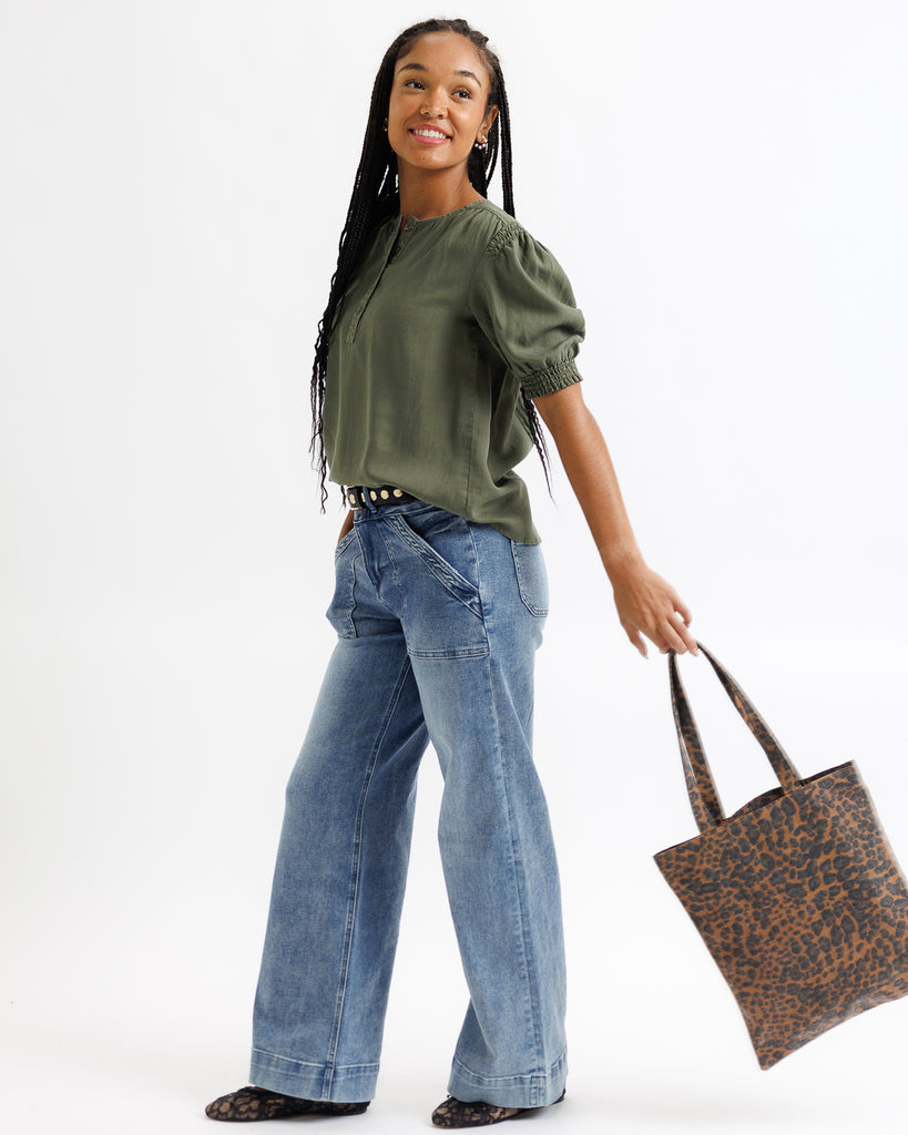 Woman wearing a green top and blue jeans, holding a brown tote bag on a white background