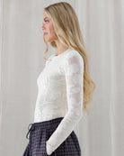 Side profile showing the slim, body-hugging silhouette, extended fitted sleeves, and delicate openwork floral knit texture of the ivory crewneck top