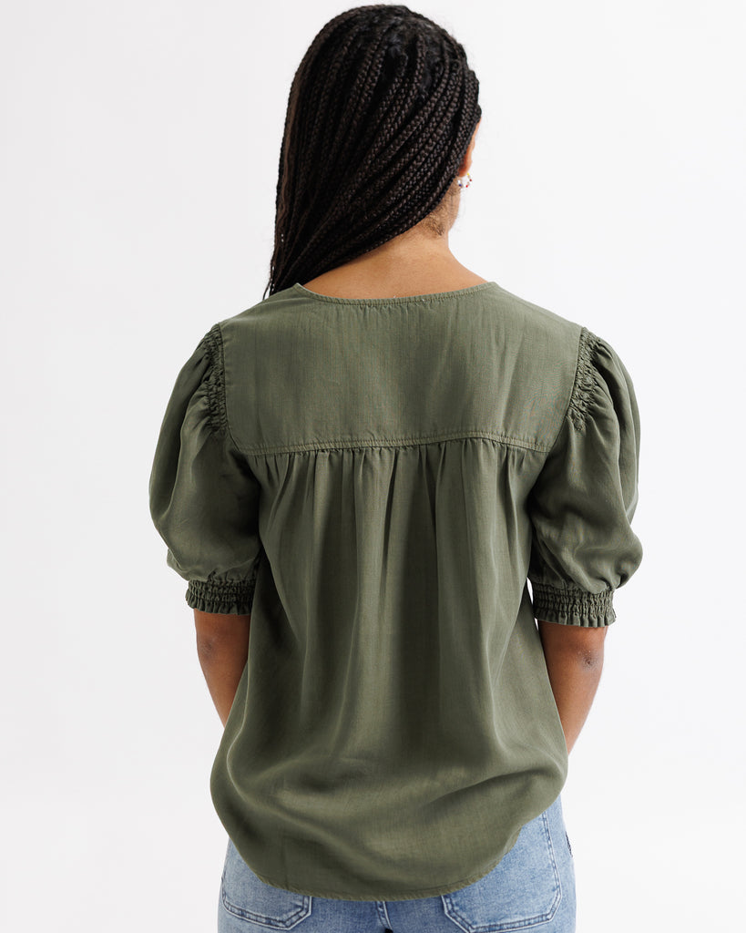 Person wearing an olive green blouse with puffed sleeves on a white background