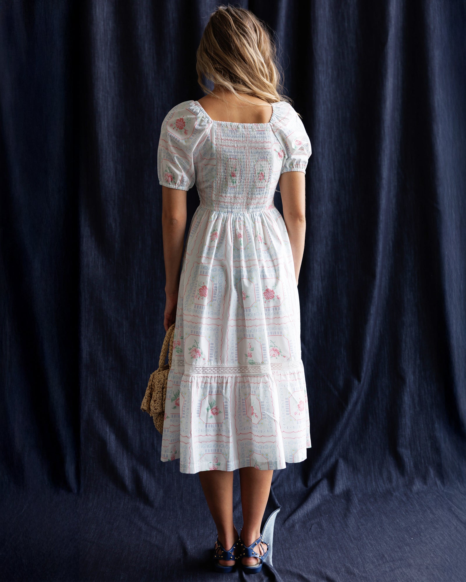 Woman wearing a white floral dress against a dark blue curtain