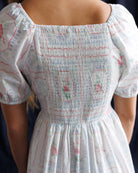 White dress with floral patterns on a person against a dark background