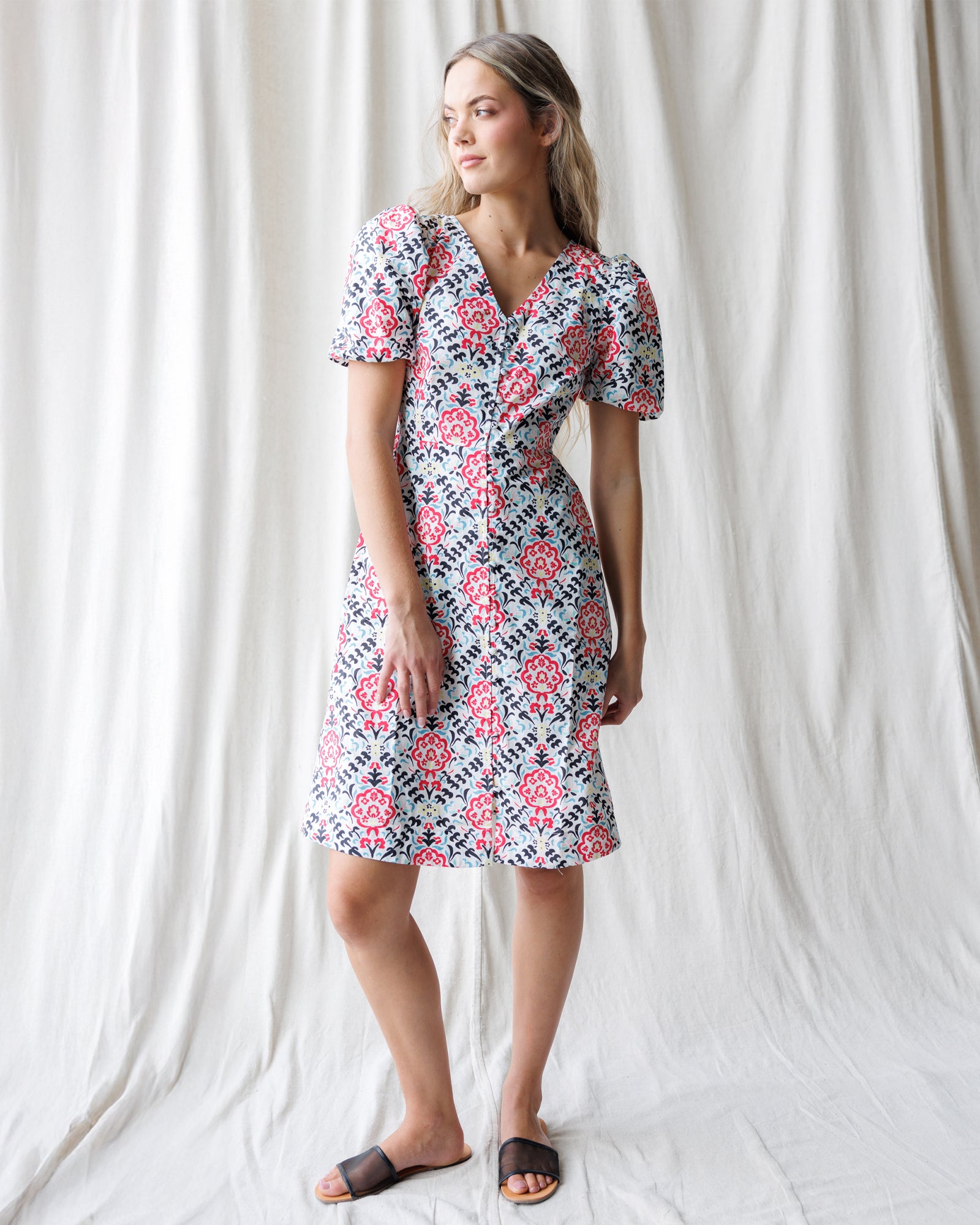 Woman wearing a floral dress standing against a white curtain