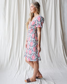 Woman wearing a floral dress standing against a white curtain.
