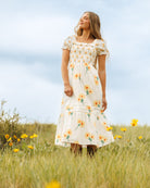 Image of woman wearing a midi dress with sunflower print standing in a field