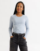 Woman wearing a light blue long-sleeve top and dark jeans on a white background