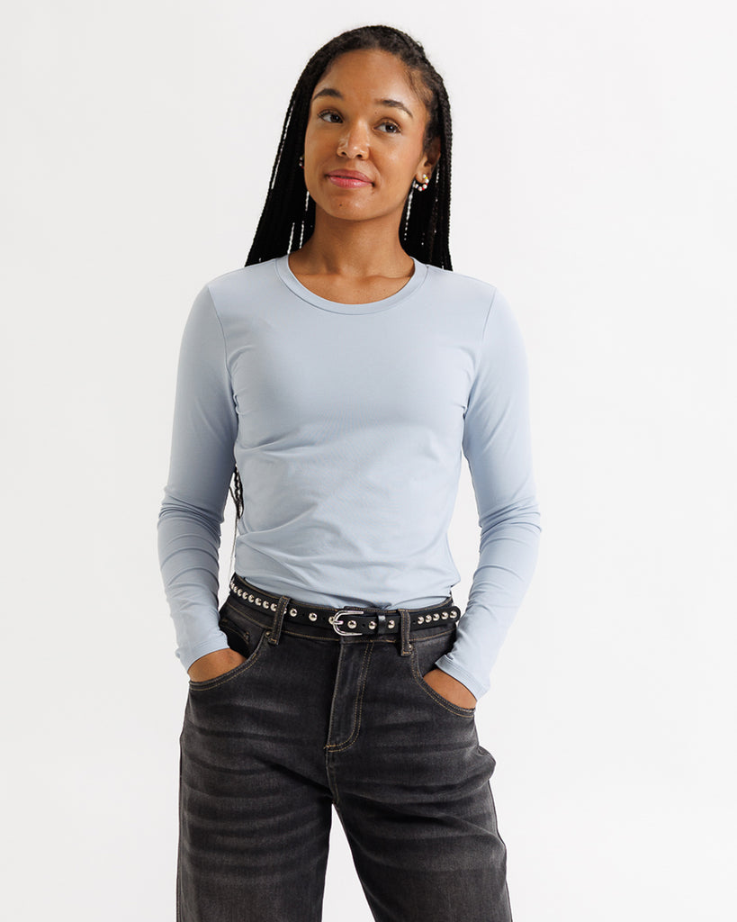 Woman wearing a light blue long-sleeve top and dark jeans on a white background