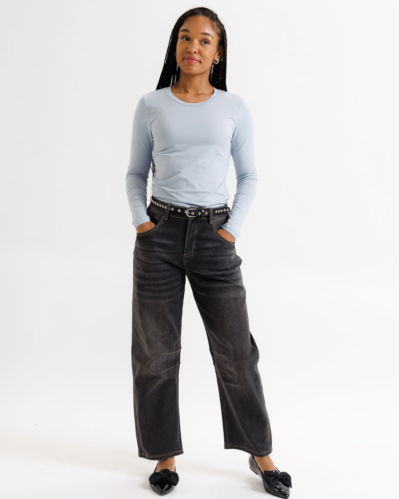 Person wearing a light blue long-sleeve top and black jeans on a white background