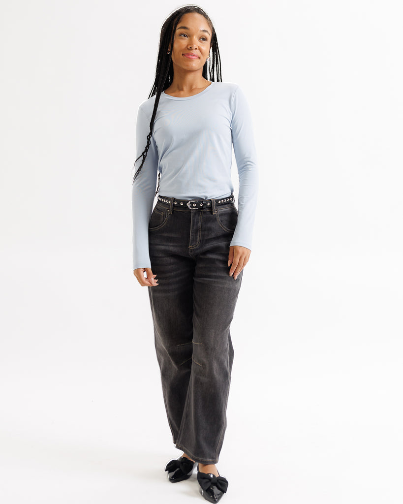 Woman wearing a light gray long-sleeve top and dark gray jeans on a white background