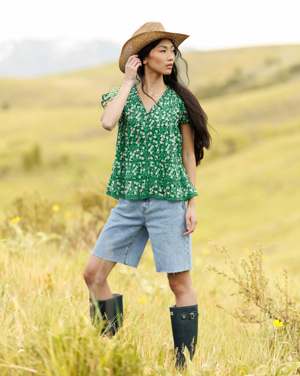 Woman wearing a green floral print blouse and denim shorts in a field