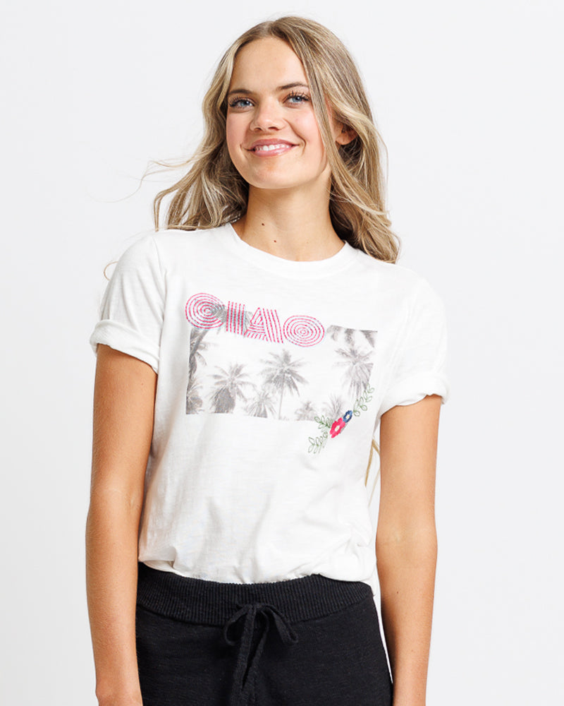 Model wearing a white short sleeve graphic tee with "ciao" and a summer scene 