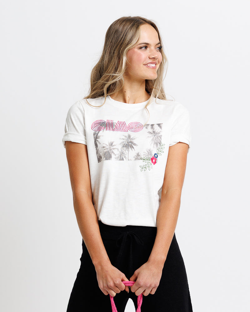 Model wearing a white short sleeve graphic tee with "ciao" and a summer scene 