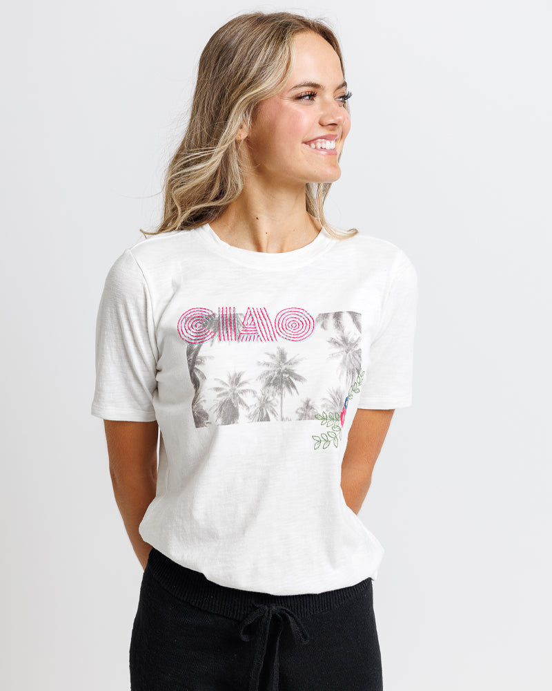Model wearing a white short sleeve graphic tee with "ciao" and a summer scene 