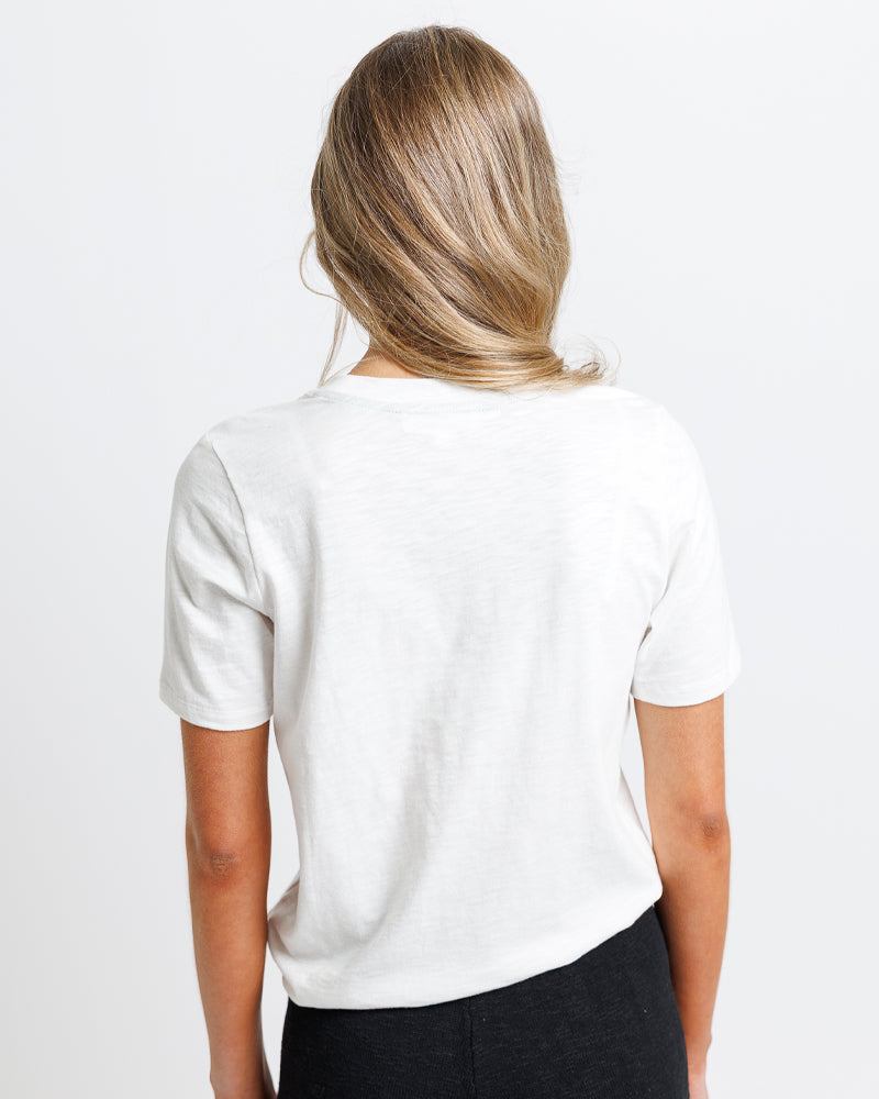 Model wearing a white short sleeve graphic tee with "ciao" and a summer scene 