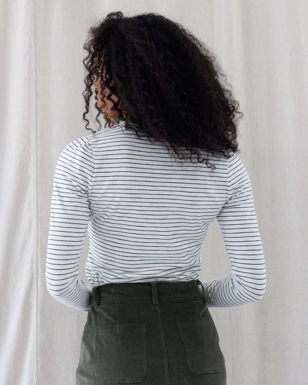 Back view showing the clean, fitted silhouette of the thin navy striped long-sleeve crewneck top and its full back coverage tucked at the waist.