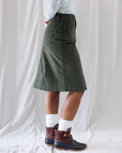 Side profile showing the clean A-line pencil fit, structured waistband, and knee-skimming straight hemline of the olive corduroy skirt.