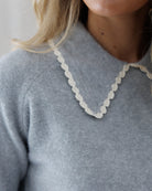 Close-up detail of the heather grey knit neckline showcasing the fine knit texture and intricate cream scalloped crochet lace along the collar edge.