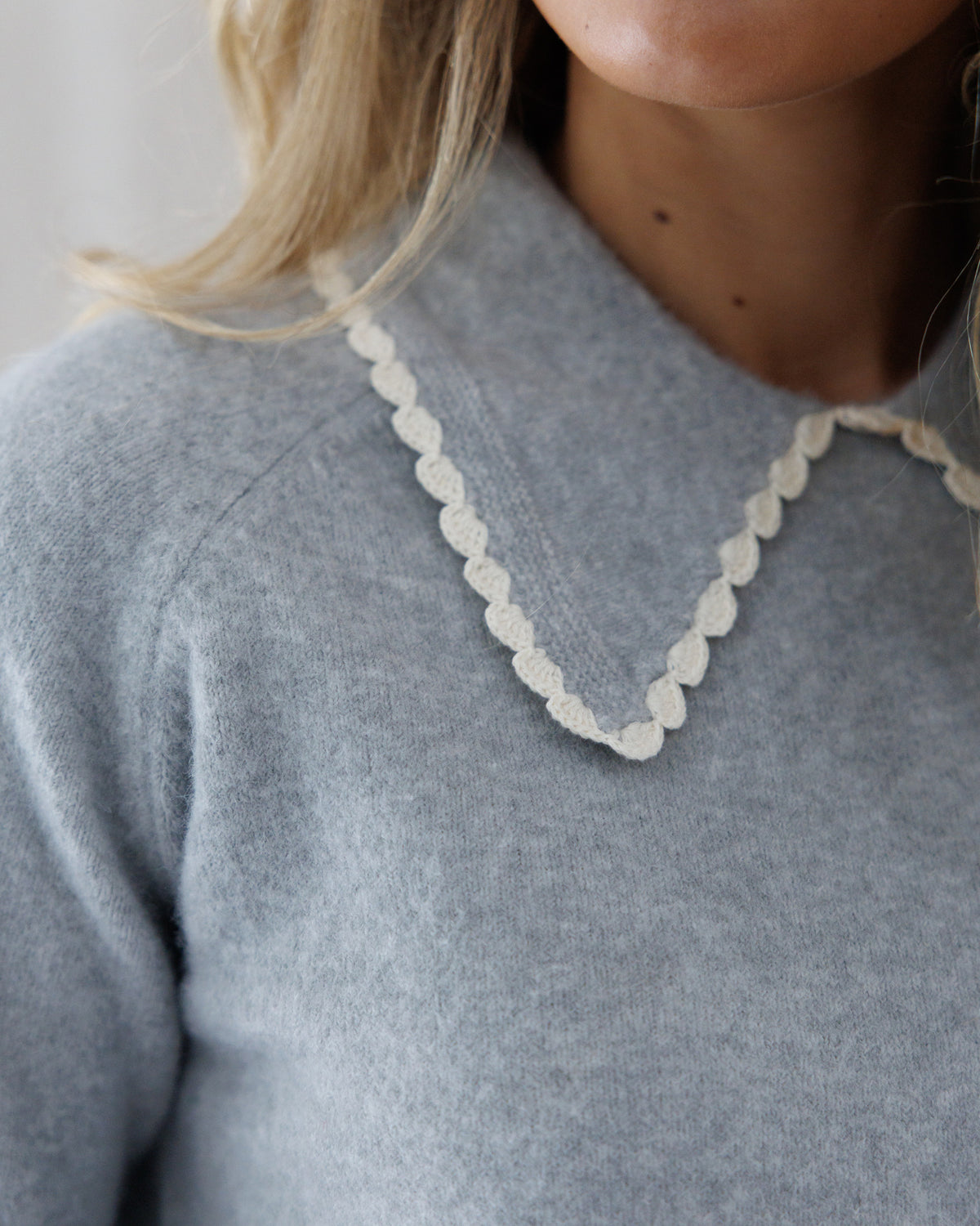 Close-up detail of the heather grey knit neckline showcasing the fine knit texture and intricate cream scalloped crochet lace along the collar edge.