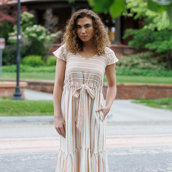 Woman in a striped dress standing outdoors with greenery in the background