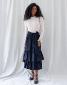 Front view showing the mid-calf silhouette of the black tiered midi skirt with a wide matching waist tie knotted at the front, paired with a tucked-in ribbed top.