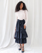 Front view showing the mid-calf silhouette of the black tiered midi skirt with a wide matching waist tie knotted at the front, paired with a tucked-in ribbed top.