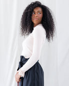Side profile showing the fitted ribbed stretch knit silhouette, gathered slight puff shoulders, and extended sleeves with contrast lace cuff detailing.