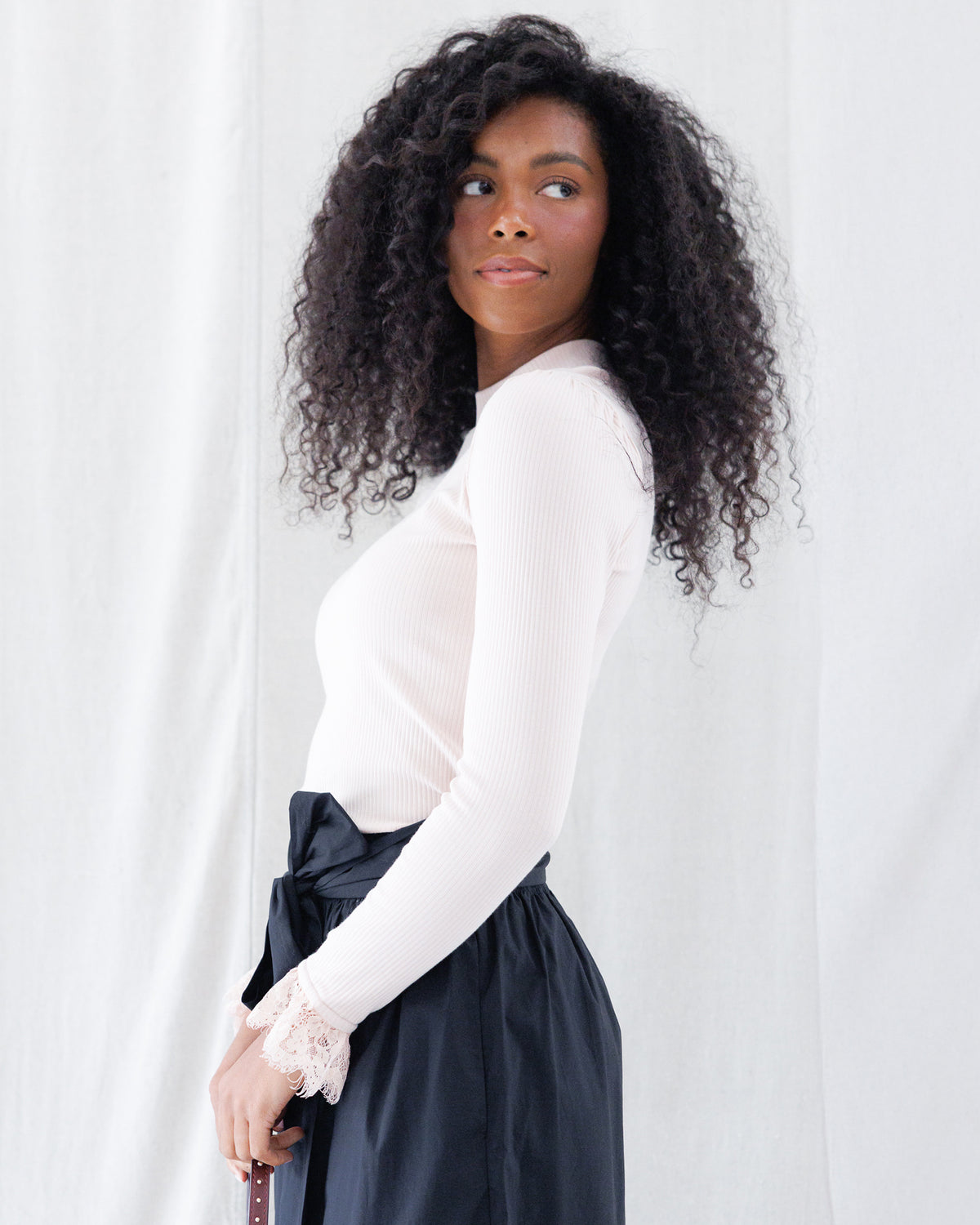 Side profile showing the fitted ribbed stretch knit silhouette, gathered slight puff shoulders, and extended sleeves with contrast lace cuff detailing.