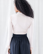 Back view highlighting the seamless fitted cut, clean ribbed texture, subtle shoulder gathering, and high mock neckline of the pale pink long-sleeve shirt