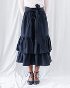 Front profile highlighting the high-rise paperbag-style waistband, statement front sash, and voluminous cascading tiers falling to midi length.