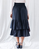 Back view displaying the gathered elastic waistband for flexible fit and the clean drape of the wide two-tier ruffled midi hemline.