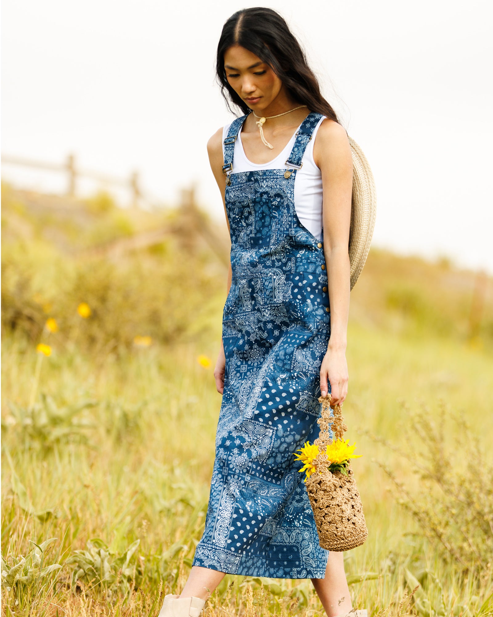 Image of woman wearing a paisley print denim overall dress standing in a field