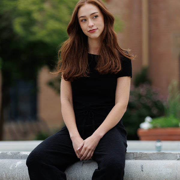 Woman in a black outfit sitting on a stone ledge with a blurred outdoor background