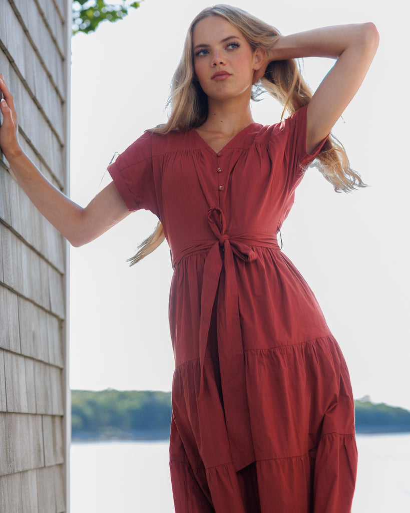 Model in a red short sleeve v-neck maxi dress standing by a wooden building with a scenic background