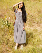 Image of woman wearing a brown gingham short sleeve dress standing in a field