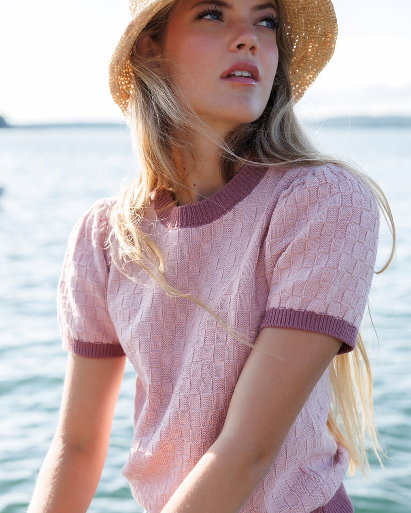 Woman wearing a pink textured dress and straw hat by a body of water