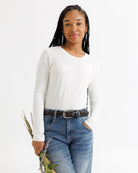 Woman wearing a white long-sleeve shirt and blue jeans holding flowers against a white background