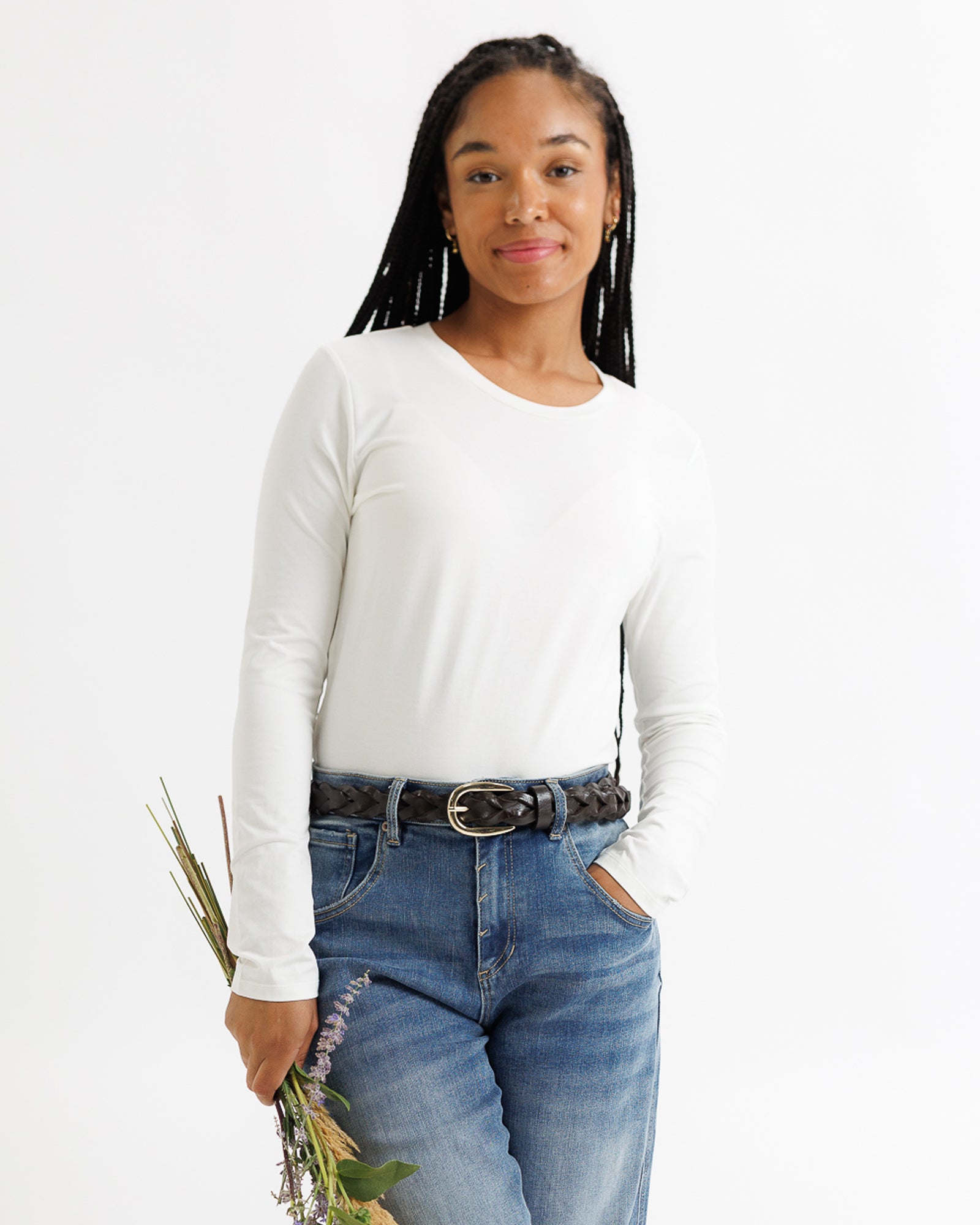 Woman wearing a white long-sleeve shirt and blue jeans holding flowers against a white background