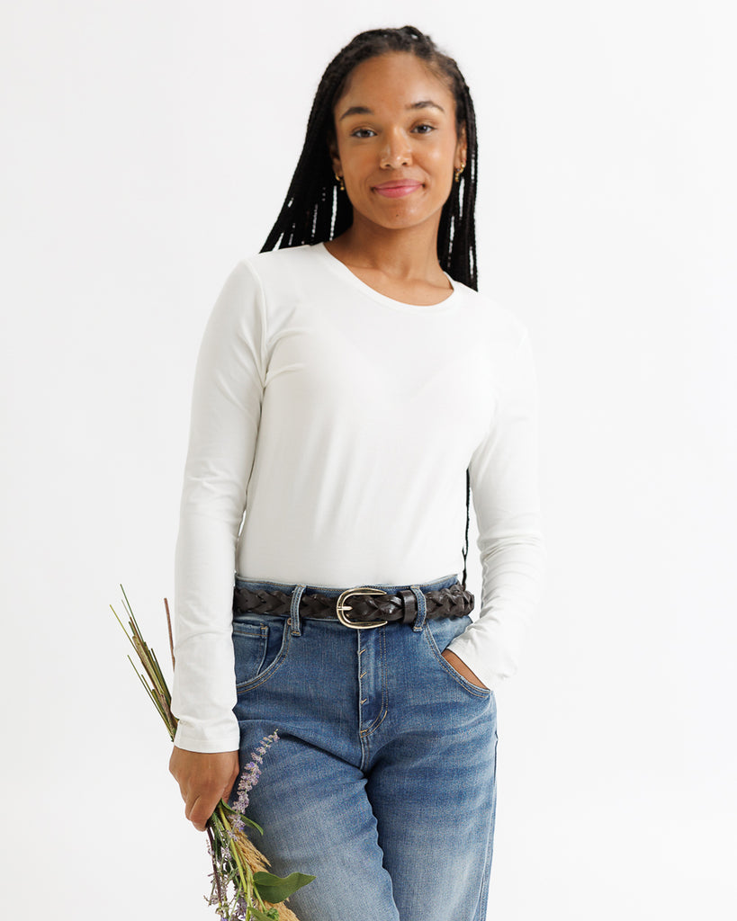 Woman wearing a white long-sleeve shirt and blue jeans holding flowers against a white background