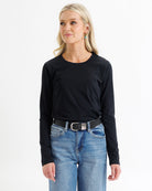 Woman wearing a black long-sleeve top and blue jeans on a white background