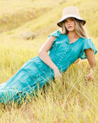 Woman wearing a teal dress and a straw hat laying in a field