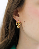 Gold bow-shaped earring worn by a person with a neutral background