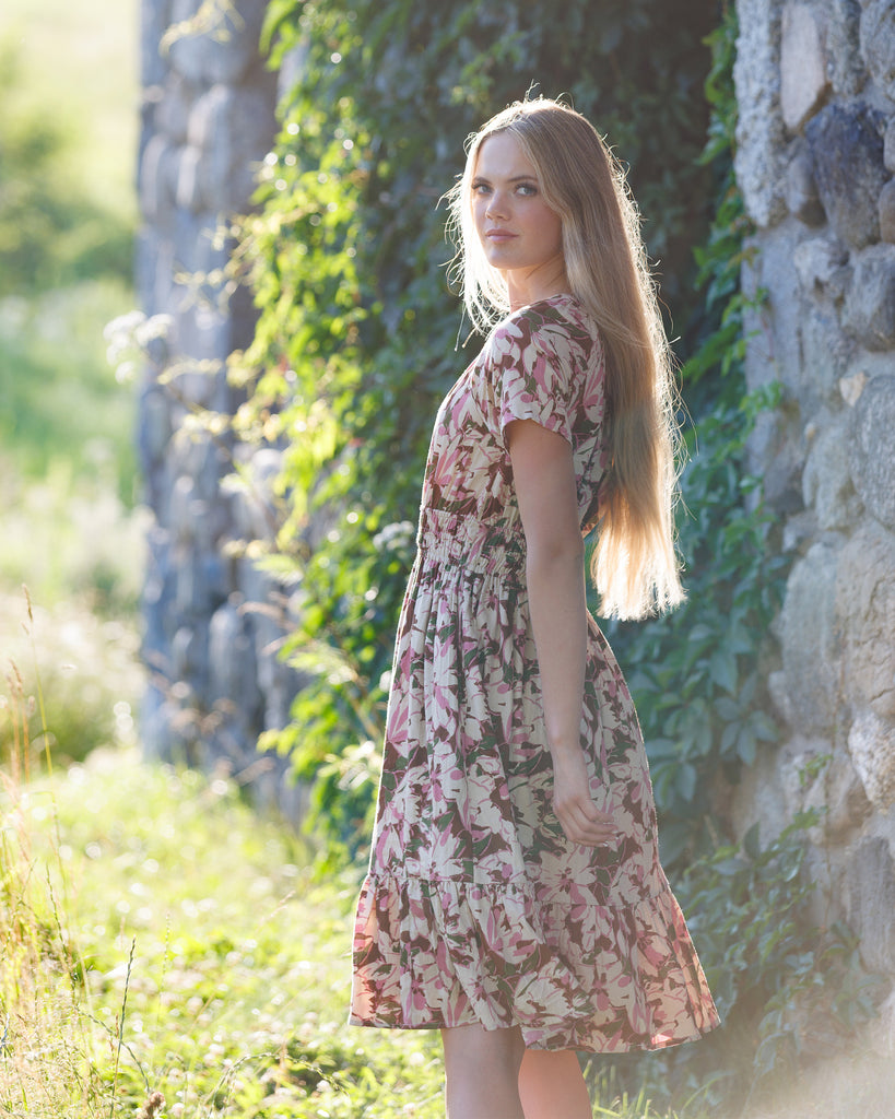 Woman in a floral dress standing against a stone wall with greenery