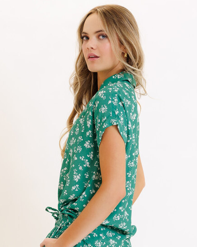 Model wearing a green with white floral print short sleeve collared button-down top