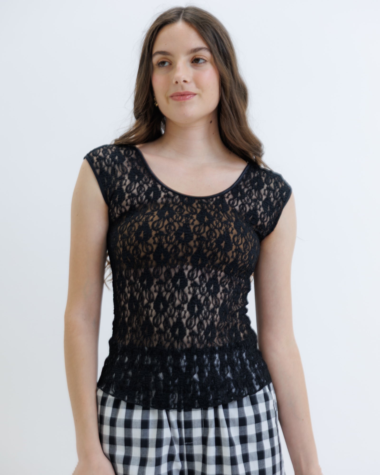 Woman wearing a black lace top and checkered pants on a white background