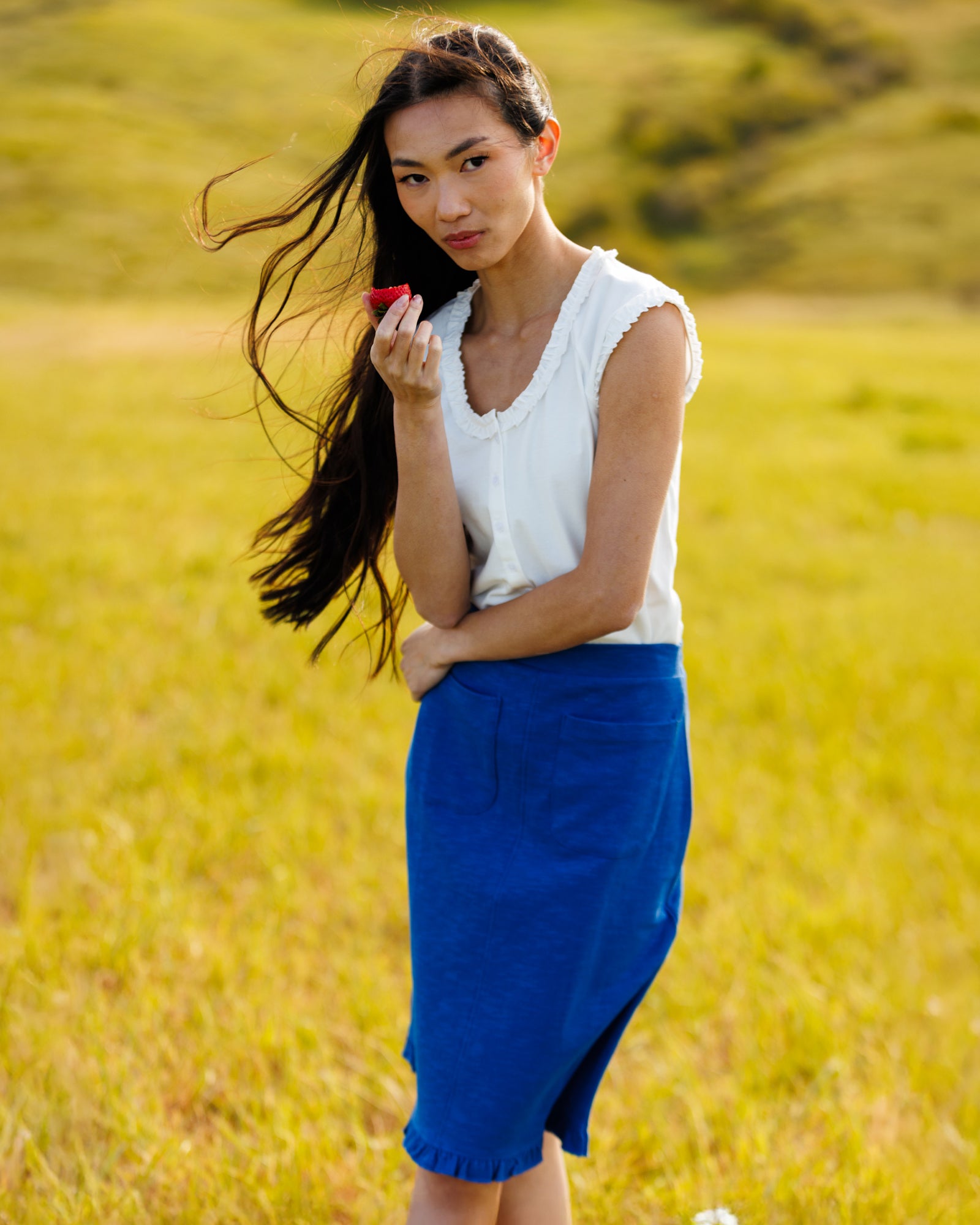 Woman wearing a white top and blue skirt in the middle of a field