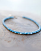 A delicate beaded bracelet with light blue and white faceted beads, resting on a textured wooden surface.