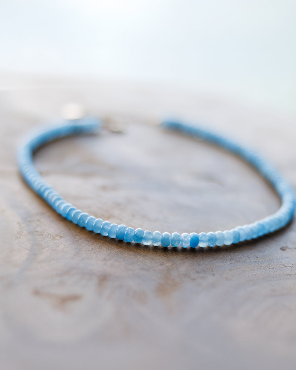 A delicate beaded bracelet with light blue and white faceted beads, resting on a textured wooden surface.